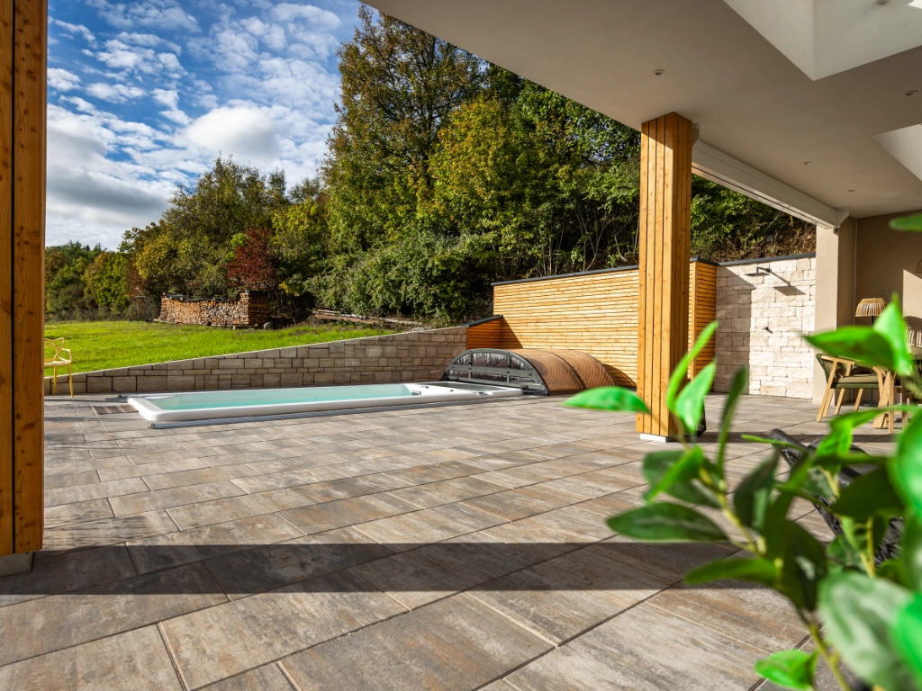 Blick auf Garten mit Pool von überdachter Terrasse, gepflastert mit Lamina 60 x 40 in der Farbe Muschelkalk